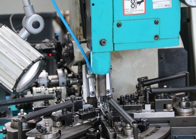 A imagem mostra uma máquina industrial especializada no fabrico e conformação de molas de torção, equipada com diversos dispositivos de guiamento, fixação e conformação do fio metálico.